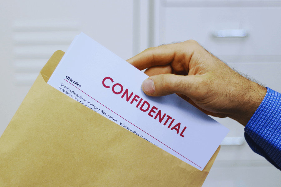 A person placing a document labeled “CONFIDENTIAL” into a brown envelope, symbolizing secure handling of sensitive information.